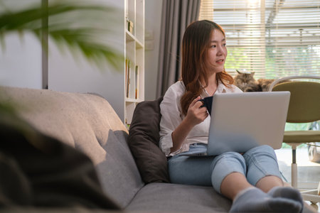 Pleasant young woman sitting on couch at home and using laptop. Technology, remote work and communication.の写真素材