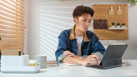 Image of young man in jean jacket browsing internet or working online on digital tablet.の写真素材