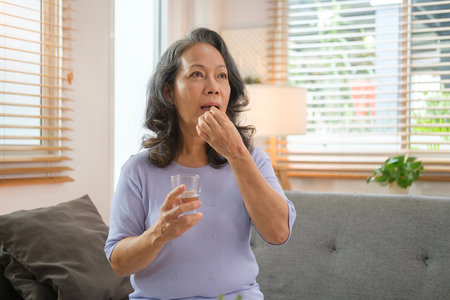 Healthy senior woman holding glass of water taking daily pill for good health. Medication, treatment and health care concept.の写真素材
