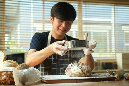 Smiling young Asian man sprinkling flour over fresh dough.の写真素材
