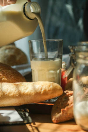 Close up view of man pouring milk into glass, preparing breakfast in kitchen.の写真素材