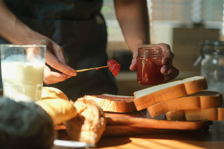 Man spreading sweet raspberry jam on toast and having breakfast at home.の写真素材