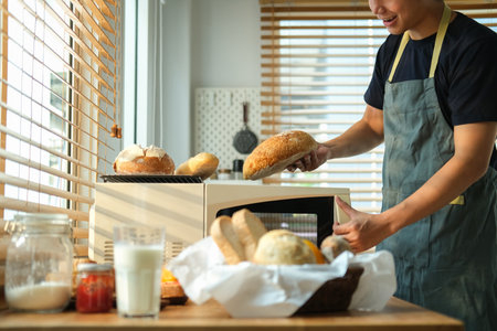 Man removing freshly baked bread from oven in kitchen.の写真素材