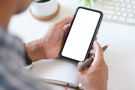 Close up view of man using smartphone at workstation. White empty screen ready for your app.の写真素材