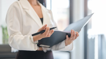 Cropped image of female office worker holding a large open binder standing in modern workplace.の写真素材