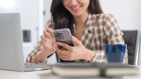 Smiling female office worker using smartphone, chatting over the internet on social networks.の写真素材