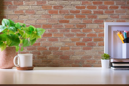 Home office desk with cup of coffee, potted plant and blank picture frame on white table.の写真素材