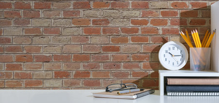 Stylish workspace with potted plant, books on white table against brick wall.の写真素材