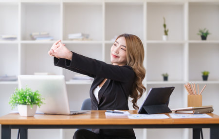 Happy female employee stretching her arms in the air, relaxing at workplace.の写真素材