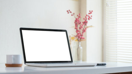 Mock up laptop computer, coffee cup and potted plant on white table. Empty screen for your advertise text.の写真素材