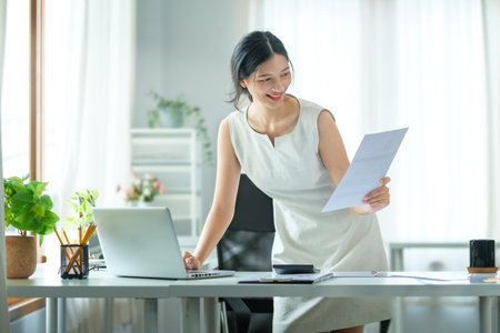 Beautiful asian businesswoman using laptop computer and checking financial document at office desk.の写真素材