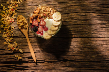 Healthy breakfast. Yogurt with granola, berries and banana on a wooden table lit by sunlight.の写真素材