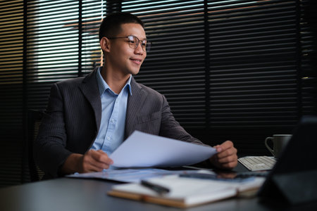 Asian businessman analyzing financial reports and using laptop at office.の写真素材