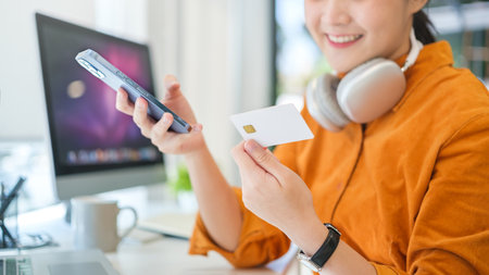 Satisfied woman holding a credit card and using smart phone. Smart payment transaction and e-commerce concept.の写真素材