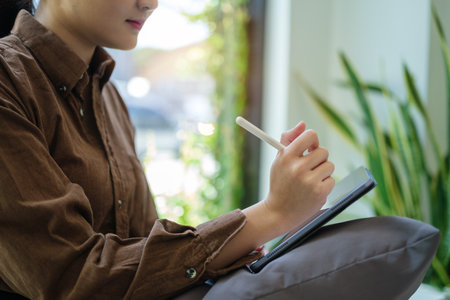 Full length of young woman in casual clothes sitting on couch and surfing internet on digital tablet.の写真素材