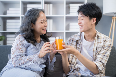 Loving elderly mother receiving
orange juice from adult son spending time together at home. Family, love and bonding conceptの写真素材