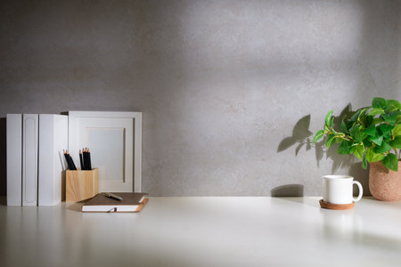 Home office interior. Houseplant, coffee cup, books and pencil holder on white table.の写真素材