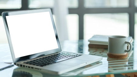 Laptop computer with blank display, cup of coffee and notebook on office desk.