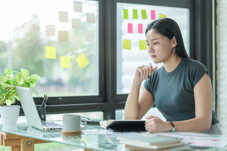 Thoughtful businesswoman reading documents while sitting in modern workplace.の写真素材