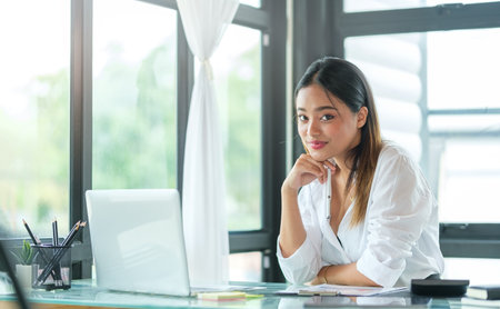 Portrait of happy young woman working on tablet pc while sitting at her working place in office.の写真素材