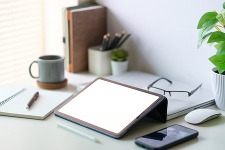 Modern workspace with a tablet computer, pot plant, notebook and coffee cup on white desk. Blank screen monitor for graphic display montage.の写真素材