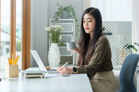 Happy young businesswoman drinking coffee and working at bright office.の写真素材
