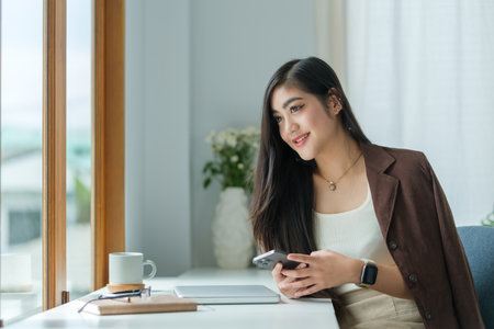 Satisfied asian young woman relaxing at her workplace and looking through the window at office.の写真素材