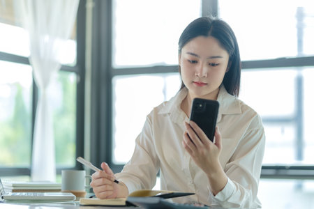 Asian female employees checking social media, reading online news on her smart phone.の写真素材