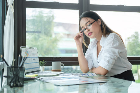 Serious businesswoman sitting in front of laptop computer at her workplace and reading financial reports.の写真素材