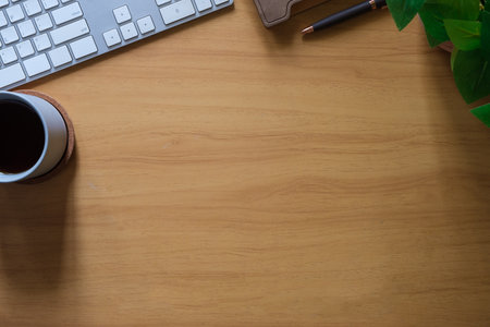 Simple workspace with keyboard, coffee cup and book on wooden table. Top view with copy space for...
