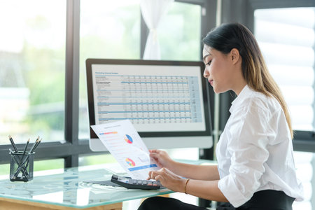 Thoughtful female entrepreneur sitting in bright modern office and checking financial reports.の写真素材