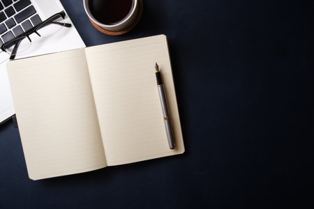Flat lay, top view of blank notebook, pen, cup of coffee, laptop and glasses on black background.の写真素材