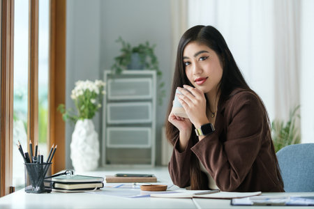 Elegant millennial businesswoman sitting in bright office and looking at camera.の写真素材