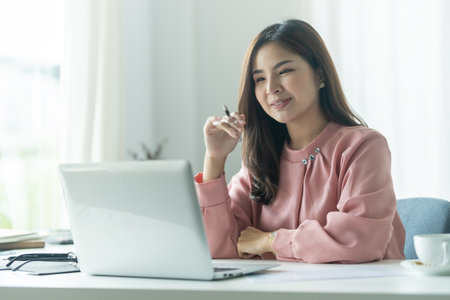 Beautiful young businesswoman looking at laptop screen, browsing internet or reading email from client.の写真素材