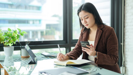 Beautiful asian businesswoman sitting at her workplace and using smart phone.の写真素材