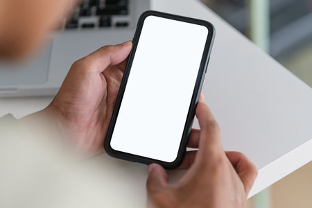 Close up view of man hands holding smart phone over working desk. Blank screen for your advertise design.の写真素材