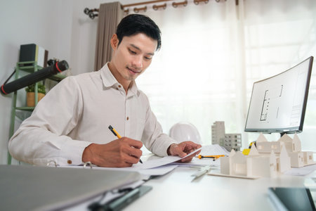 Side view of smiling young architect in shirt working on blueprints at bright modern office.の写真素材