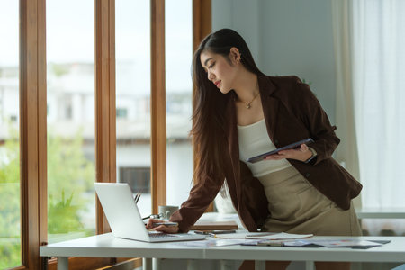 Thoughtful asian businesswoman checking financial reports at her office desk.の写真素材
