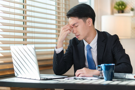 Tired businessman massaging nose bridge, fatigued from computer work.の写真素材