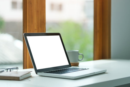 Laptop computer with blank display, cup of coffee and notebook on office desk.の写真素材
