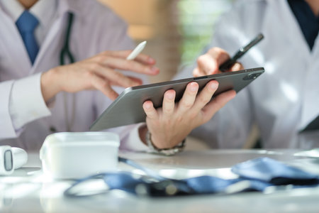 Two general practitioners discussing illnesses treatment or health test results on digital in medical office.の写真素材