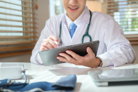Doctor in white medical coat and stethoscope using digital tablet at clinic office. Medical and healthcare concept.の写真素材