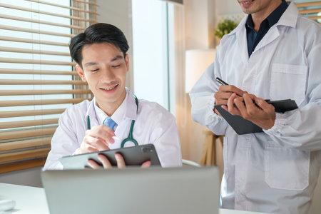 Two general practitioners discussing illnesses treatment or health test results on digital in medical office.の写真素材
