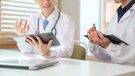 Two general practitioners discussing illnesses treatment or health test results on digital in medical office.の写真素材