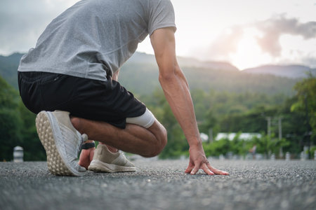 Athlete asian man in running start pose on the city street. Sport tight clothes Bright sunset.