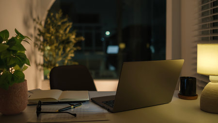 Laptop, financial documents, glasses and coffee cup on white desk in dark roomの写真素材