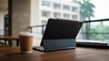 Digital tablet and paper cup of coffee on wooden table at cafe. Remote working concept.の写真素材