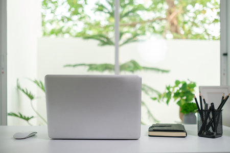 Laptop computer on white table near window with view of garden.の写真素材