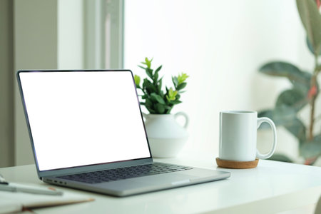 Laptop with empty display, potted plant and coffee cup on white table in home office.の写真素材