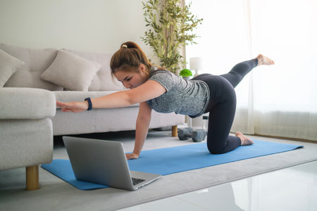 Young Asian woman in sportswear practicing yoga, doing balancing table top pose on mat at home.の写真素材